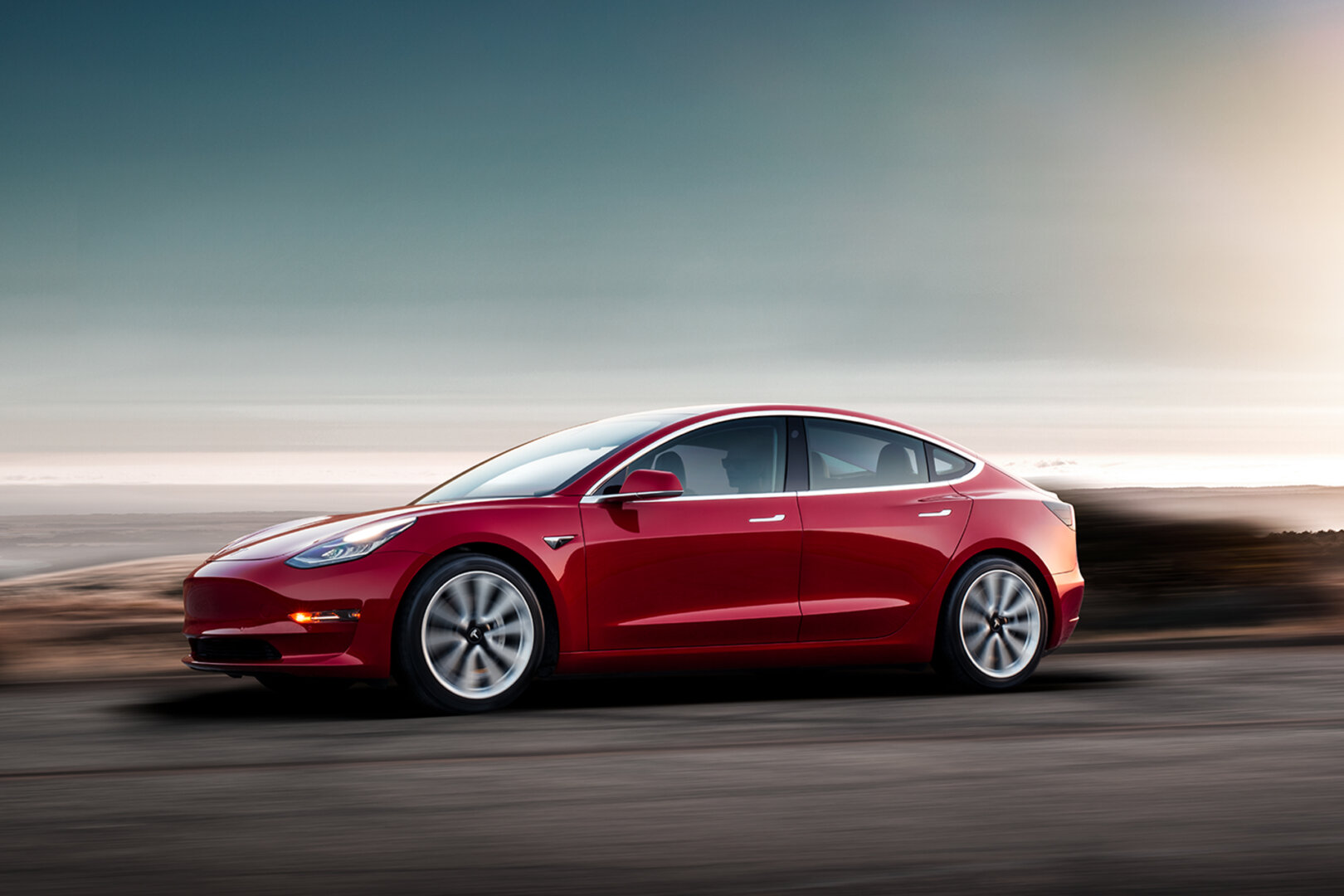 Roter Tesla Model 3 in rot fährt eine Straße entlang