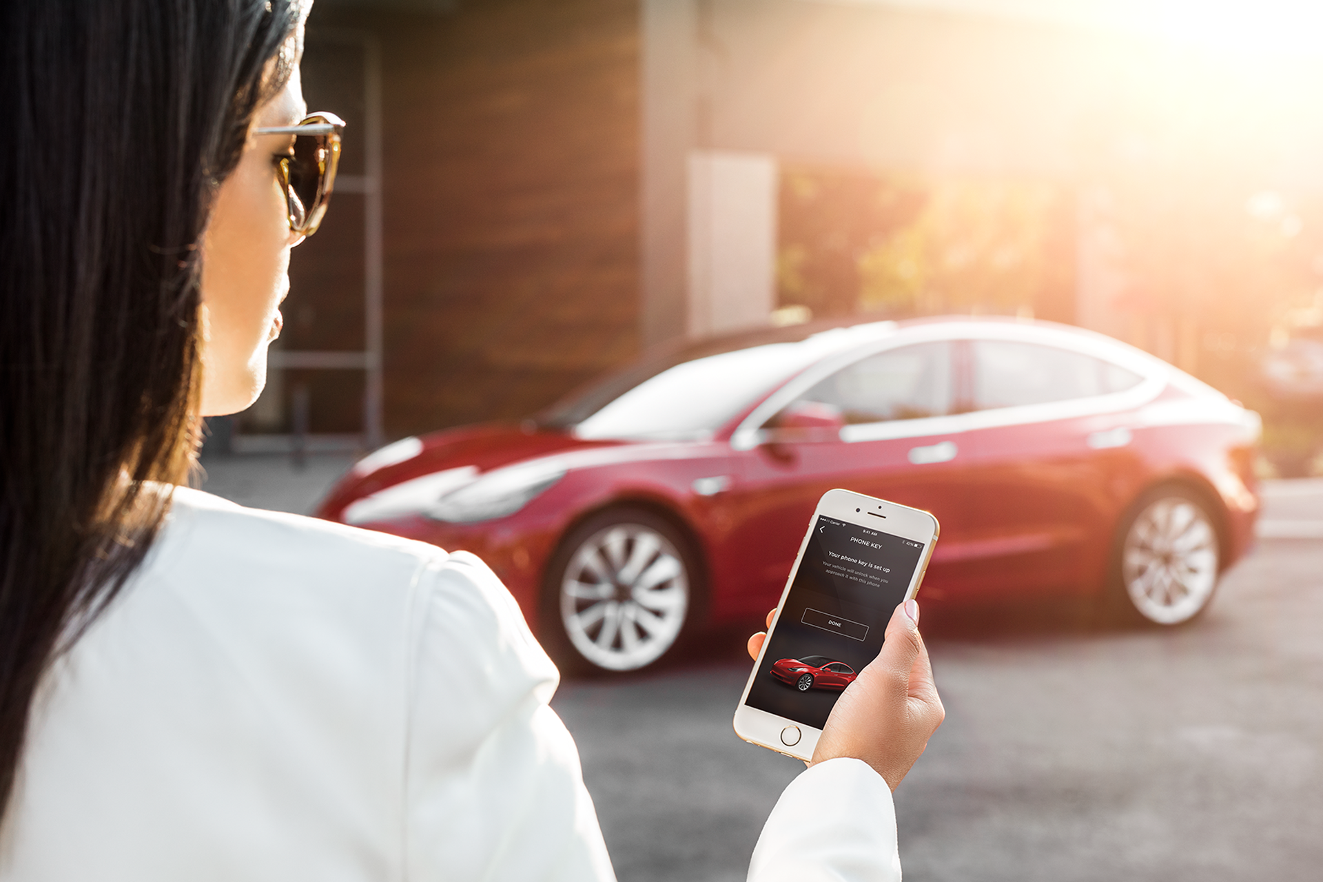 Frau schaut auf App im Handy, die Tesla Model 3 steuert