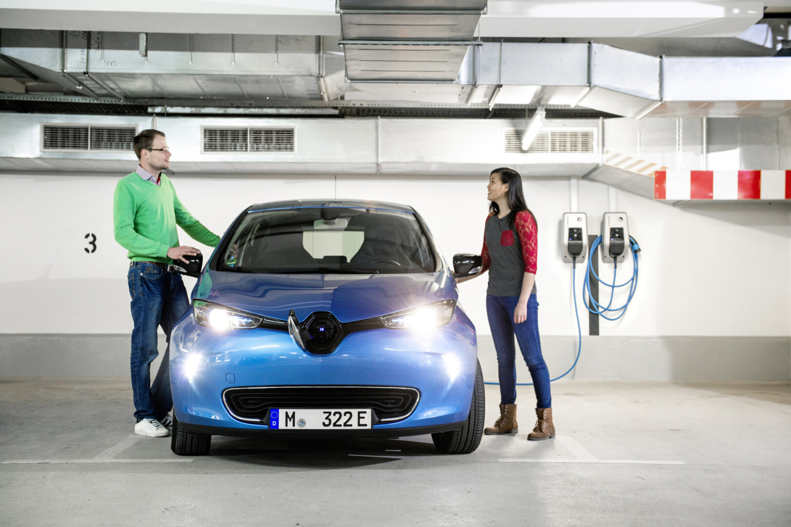Frau und Mann stehen an blauem Renault Elektroauto während es an Wallbox lädt