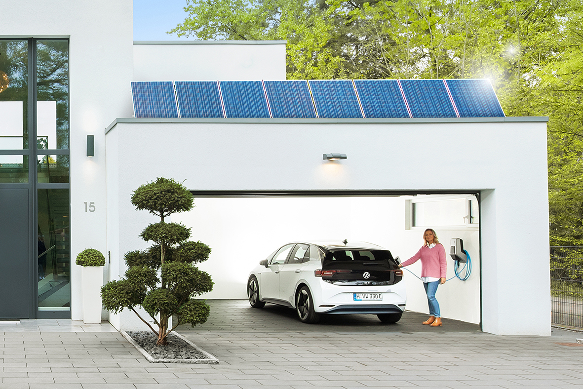 Frau lädt ihr weißes Elektroauto in ihrer Garage mit Solaranlage darauf.